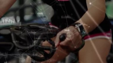 Sarışın, beyaz bir kadının arka plandaki spor salonunda statik bir bisikletle gülüp spor yaptığı bir bağlantı ağının, veri işleme ve analizlerinin animasyonu.