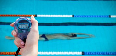 Sudaki yüzücüye karşı performansı ölçmek için kronometre tutan bir kadının yakın çekimi.