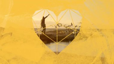 Gün batımında kollarını kumsalda sallayan bir adamın animasyonu. Gün batımında deniz üzerinde uçan bir kuş sürüsü. Ön planda sarı kalp şeklinde bir pencereden görülüyor.
