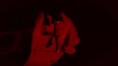 Kadın ellerinin animasyonu, kırmızı ışıkla dolu dua jesti ile birbirine yapışmış, siyah zemin üzerinde ağır çekimde çalışan elektrikli matkabı kapatmış.. 