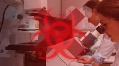 Kırmızı sağlık tehlike işaretinin animasyonu, kimyasal bileşiklerin çapraz ve yapısal formülleri ve Coronavirus Covid-19 arka plandaki laboratuvarda mikroskopla çalışan erkek ve kadın bilim adamları üzerinde yayılıyor.. 