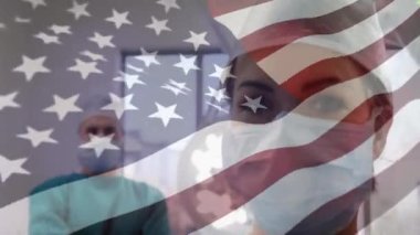 Amerikan bayrağının koruyucu giysiler ve yüz maskesi takan erkek ve kadın doktorların ameliyat odasında dikilip arka plandaki kameraya baktığı animasyon.. 