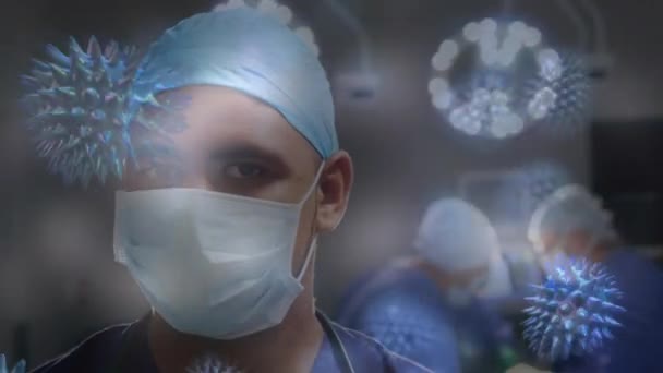 背景のカメラを見ると 手術室に身を包んだ男性医師の上に広がる巨大なコロナウイルスCovid 19細胞のアニメーション — ストック動画