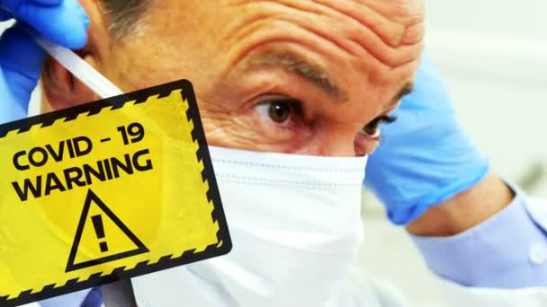 顔のマスクを背景に男性医師の上に黄色と黒の看板に書かれた黒のCovid 19警告記号のアニメーション — ストック動画