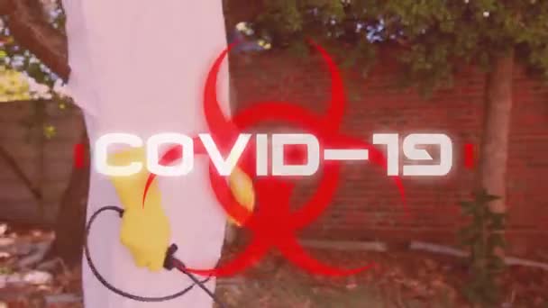 コヴィッド という言葉のアニメーションは 庭に立って保護服を着た男が背景で笑顔で健康被害の兆候に白い文字で書かれています 医学公衆衛生パンデミックコロナウイルスCovid 19発生概念デジタル複合体 — ストック動画