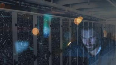 Kapüşonlu bir adamın bilgisayarı hacklemesi, veri işleme ve dijital bilginin sunucu odasındaki bilgisayar sunucularından geçişi ve yüzeyde ışık izleri olması.. 