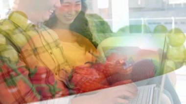 Asyalı bir çiftin dizüstü bilgisayar kullanarak arka planda duran bir kasede duran sebze ve meyvelerin üzerinde kredi kartı taşıdığı animasyon. Karantina karantinasında sosyal uzaklık ve kişisel izolasyon dijital kompozit.