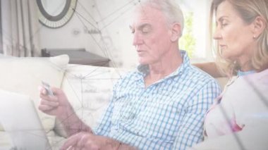 Kanepede oturan yaşlı beyaz bir çiftin dizüstü bilgisayarlarını arka plandaki bağlantıları üzerinden kullandıkları animasyon. Karantina karantinasında sosyal uzaklık ve kişisel izolasyon dijital kompozit.