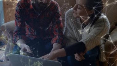 Kafkasyalı bir çiftin kanepeye oturup dizüstü bilgisayar kullanması ve arka plandaki bağlantıların üzerinden kredi kartı tutması. Karantina karantinasında sosyal uzaklık ve kişisel izolasyon dijital kompozit.