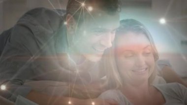 Kanepeye oturmuş, dizüstü bilgisayar kullanan beyaz noktalardan oluşan bir ağ üzerinden kameraya doğru giden beyaz bir kredi kartı tutan beyaz bir çiftin animasyonu. Karantina karantinasında sosyal uzaklık ve kişisel izolasyon dijital kompozit.