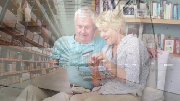 カウチスチに座っているシニア白人夫婦のアニメーション 背景に倉庫の上にノートパソコンを使用して 隔離ロックダウンデジタル複合体における社会的距離と自己分離 — ストック動画