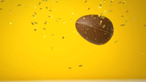 チョコレートのアニメーションイースターエッグが落ち 黄色の背景に金色のコンフェッティが飛んでいます イースターお祝いの伝統的なコンセプトデジタル生成画像 — ストック動画
