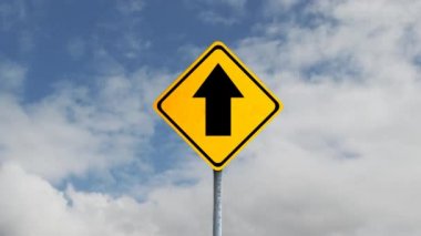 Siyah oklu sarı yol işaretinin animasyonu, arka planda tekrarlanan hareketlerle gökyüzünde hızla hareket eden beyaz bulutlar. Hareket kopyalama alanı ve tekrarlama zamanaşımı kavramı dijital olarak oluşturulmuş resim.