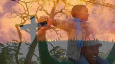 Hristiyan haçı, oğlunu sırtında taşıyan mutlu bir baba, hızlı hareket eden turuncu bulutlar ve arka planda ağaçlar. Paskalya dini kavramı dijital kompozit.