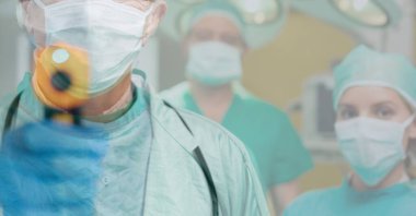 Koruyucu giysi, eldiven ve yüz maskesi takan, yüz maskesi takan, arka plandaki kameraya bakan, yüz maskesi takan iki doktorun üzerinde elektronik termometre tutan bir doktorun dijital çizimi..