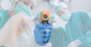 Yüz maskesi takan bir doktorun dijital çizimi, arka plandaki kameraya bakan, yüz maskesi takan ve koruyucu elbiseler giyen birçok doktorun üzerinde elektronik termometre tutan bir doktor..