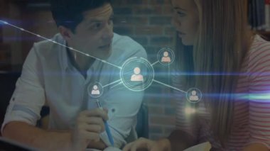 Kafkasyalı bir çiftin masa başında oturup arka planda yayılan bağlantılar ağı üzerinden evrak işlerini tartışması..