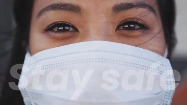 言葉フェイスマスクを着用してアジアの女性の上に書かれた安全な滞在 公衆衛生パンデミックコロナウイルスCovid 19隔離ロックダウンコンセプトにおける社会的距離と自己隔離デジタル複合体 — ストック動画
