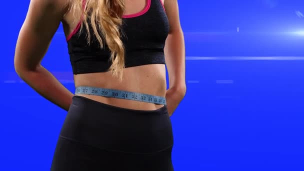 一名身穿运动服的健康白人妇女的中间部分用胶带测量腰围 而蓝色背景则用镜头耀斑和数字合成 — 图库视频影像