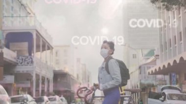 Covid-19 kelimelerinin animasyonu Asyalı bir kadının üzerinde süzülüyor yüz maskesi takıyor, sokakta bisikletle yürüyor. Coronavirus Covid-19 pandemik konsept dijital bileşik