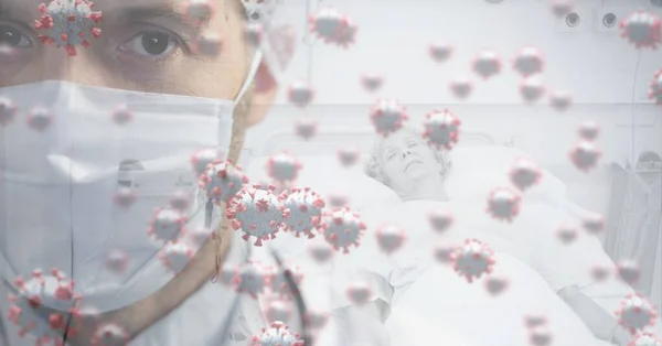 图片中的巨细胞Covid 19漂浮在一位戴着面具 站在病人床边的高加索男医生身上 Coronavirus Covid 19大流行病概念数字组合 — 图库照片