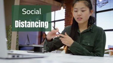 Ofiste oturan ve çalışan Asyalı bir kadında dizüstü bilgisayar ve kalem kullanan Sosyal Mesafe animasyonu. Karantina karantinasında kişisel izolasyon.