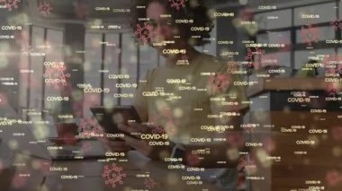 COVID-19 kelimelerinin animasyonu ve evdeki bilgisayar ve tablet kullanarak melez ırk adamlarının üzerinde yüzen virüs ikonları. Karantina karantinasında kişisel izolasyon dijital kompozit
