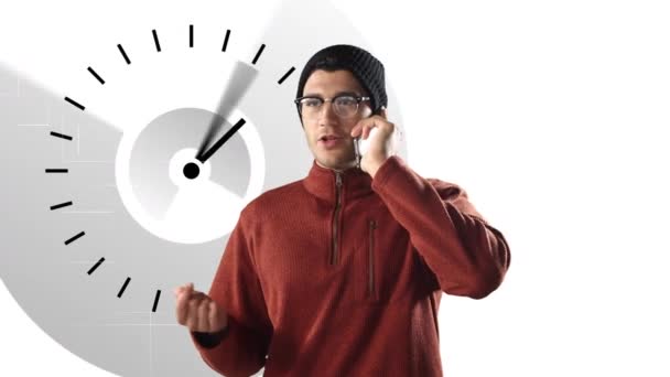 ビーニーと眼鏡をかけ 笑顔で白い時計のアイコンを背景にスマートフォンで話している混合レースマンのアニメーション 世界経済と技術の概念デジタル複合体 — ストック動画