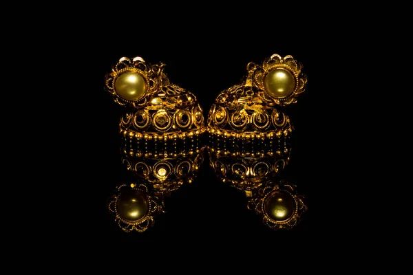 Earring Gold Jewelry Traditional With Stones and Two Golden earrings with reflection . Pair of golden earring with pearl tone on black background. Luxury female jewelry, close-up