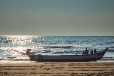 Aile üyeleri gündoğumu deniz manzarasında huzur içinde vakit geçiriyorlar. Aile teknede oturuyor.