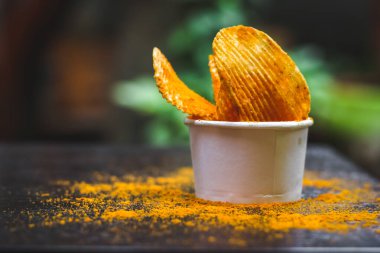 Cipsler, acılı ve baharatlı patates cipsleri yeşil bitki arkaplanlı masada yemeye hazır..