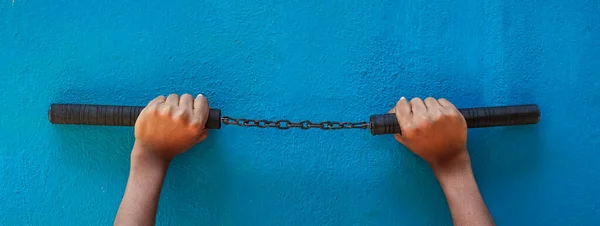 Nunchaku holding on hand isolated on Blue background. Black nunchaku training for beginner. Hot Tactical Gear Martial Arts Equipments.