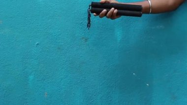 Mınçıka eğitimi. Mavi arka planda yalnız başına nunchaku pratiği yapan yetişkin bir çocuk..
