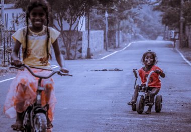 Chennai, Hindistan, 20 Ocak 2018: Yol kenarındaki küçük kızlar sokakta oynuyorlar ve utanıyorlar. Sokakta bisiklet süren kız çocuğu.