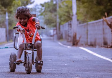 Chennai, Hindistan, 20 Ocak 2018: Yol kenarındaki küçük kız sokakta oynuyor ve utanıyor. Kız sokakta bisiklet sürüyor..
