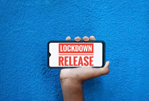 Lock down release wording on smart phone screen isolated on blue background with copy space for text. Person holding mobile on his hand and showing front screen. Lock down release for corona virus .