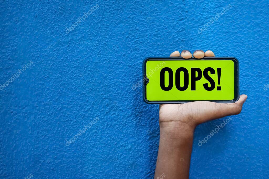 OOPS wording on smart phone screen isolated on blue background with copy space for text. Person holding mobile on his hand and showing front of the screen wording oops..