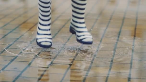 Meisje in rubber laarzen loopt en springt in een plas — Stockvideo