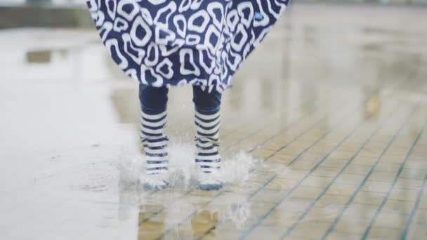 Дівчина в гумових чоботях бігає і стрибає в калюжу — стокове відео