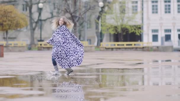 Девушка в резиновых сапогах бежит и прыгает в лужу — стоковое видео