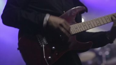 Gitarist konser sahnesinde yavaş çekimde elektro gitar çalıyor.