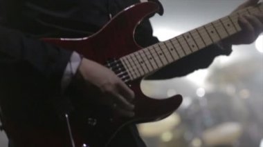 Gitarist konser sahnesinde yavaş çekimde elektro gitar çalıyor.