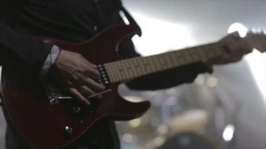 Gitarist konser sahnesinde yavaş çekimde elektro gitar çalıyor.