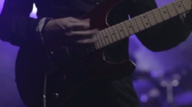 Gitarist konser sahnesinde yavaş çekimde elektro gitar çalıyor.