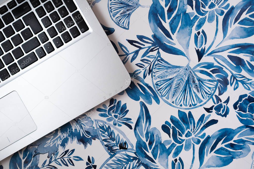 Flat lay of a laptop in a blue and white floral background, small business working