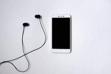Beyaz arka planda siyah kulaklıklı bir cep telefonu. Müzik dinlemeye hazır. Düz yatıyordu