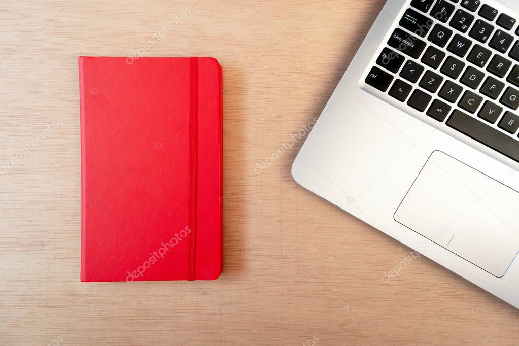 Laptop on wooden desk with a red notebook, flat lay, top view, workspace