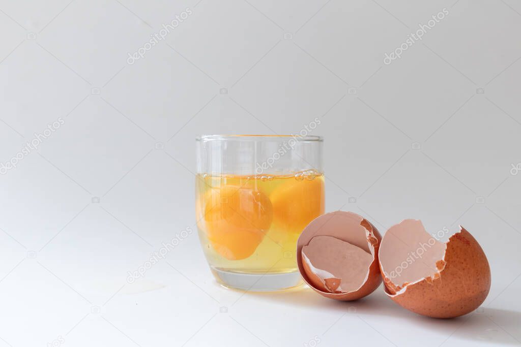 Broken eggs in a glass jar with its eggshells in white background, copy space