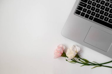 Dizüstü bilgisayarı, çiçekleri ve beyaz arkaplanda kopyalama alanı olan çalışma alanının üst görünümü
