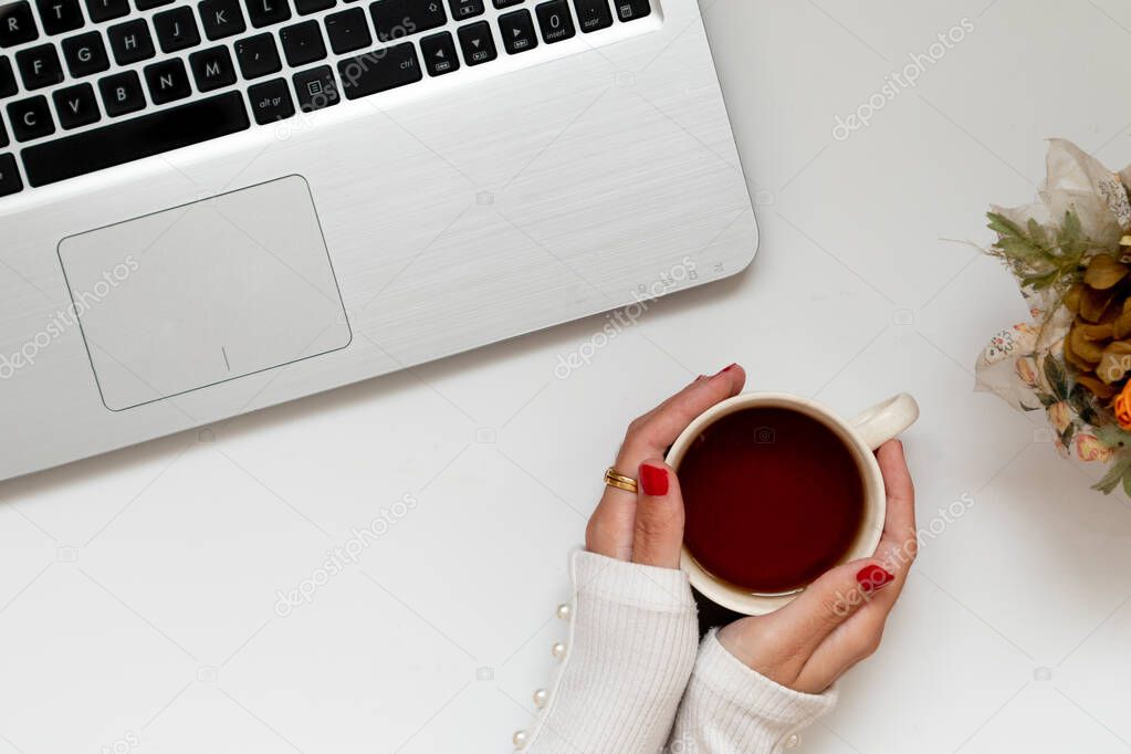 Girl hands around a coffee cup, with laptop, workspace. Flat lay composition, top view